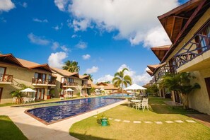 A hotel with a swimming pool, outdoor seating, and palm trees. - Pousada Rangai (Maragogi)