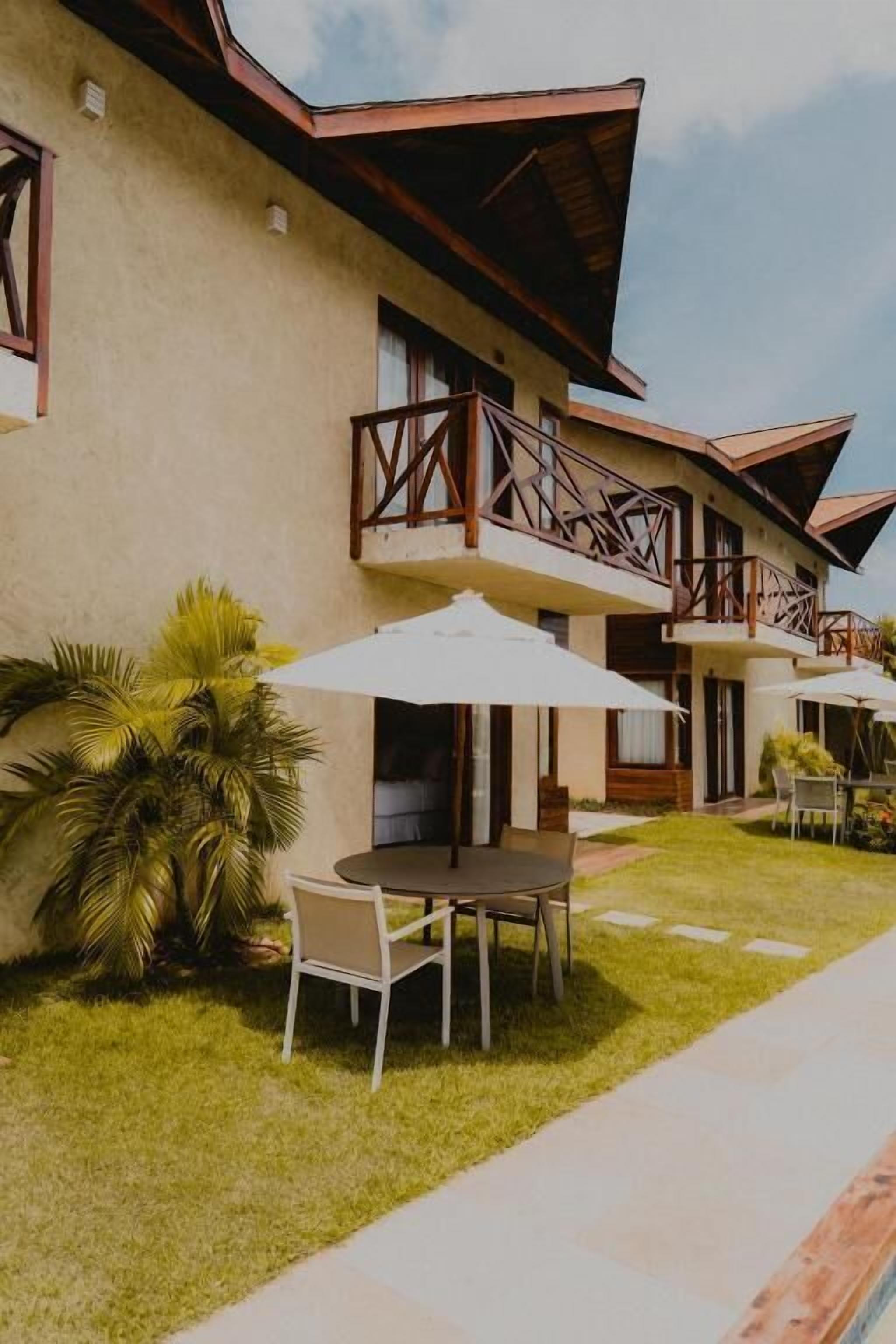 Um edifício com varanda, mesa e cadeiras, e um guarda-sol branco.