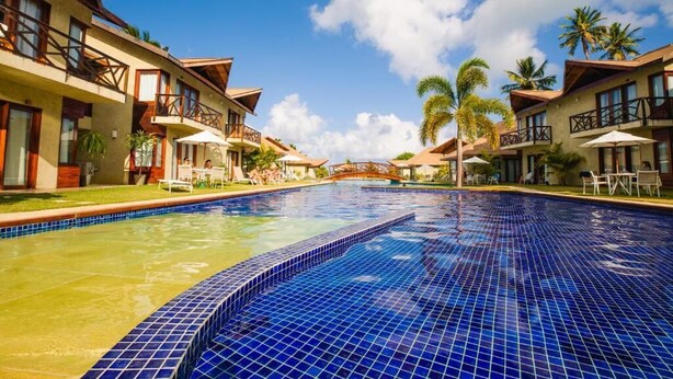 A hotel with a swimming pool, balconies, and palm trees. - Pousada Rangai (Maragogi)