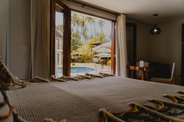A room with a large bed, a view of a pool and palm trees, a desk, and a chair.