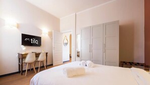 Ein Hotelzimmer mit einem Bett, einem Schreibtisch mit Stühlen, einem Kleiderschrank und einem an der Wand befestigten Fernseher.