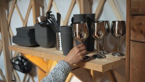 Una estantería de madera con platos apilados, un termo y copas de vino.