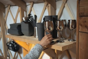 Una estantería de madera con platos apilados, un termo y copas de vino.