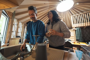 A rustic interior with wooden beams, a kitchen area, and a dining space. - Cozy Yurt in the Woods (Sainte-Agathe-des-Monts)