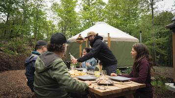 Un grupo de personas sentadas en una mesa de picnic de madera al aire libre, con una tienda de campaña al fondo.