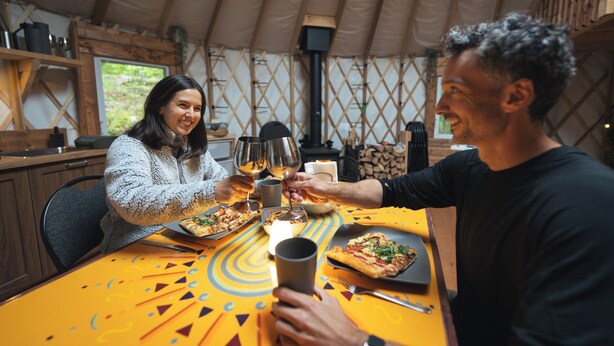 Una mesa de comedor con pizza, copas de vino y una vela.