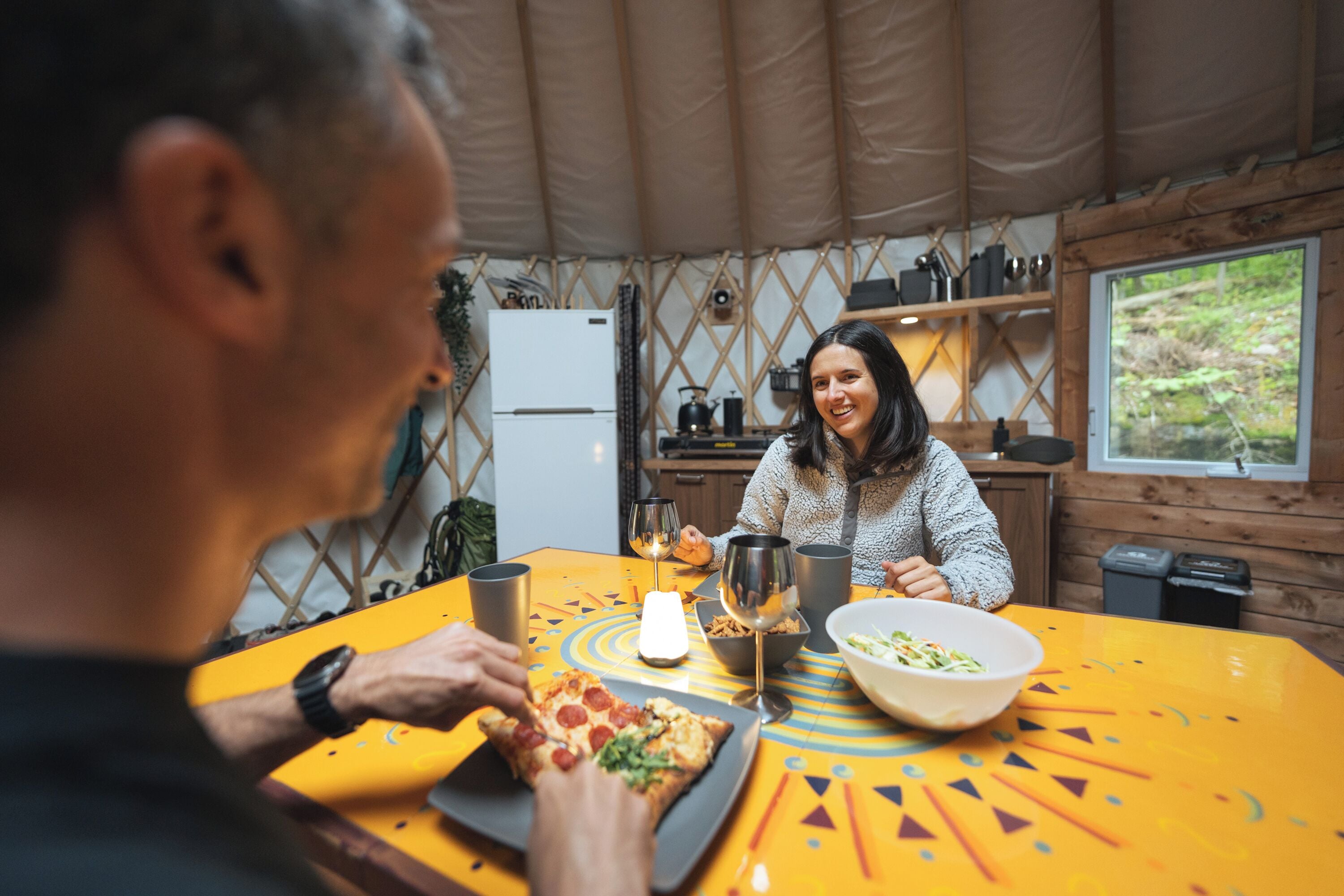 Un coin repas avec une table jaune, une pizza et un saladier rempli de salade.