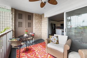 A balcony with a dining table, chairs, a sofa, and a ceiling fan. - Alii Villas#221 (Kailua-Kona)