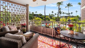 A balcony with wicker furniture, a ceiling fan, and a view of a pool and palm trees.