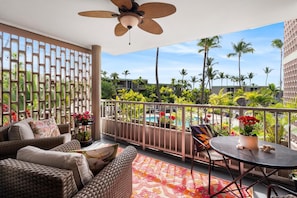 A balcony with wicker furniture, a ceiling fan, and a view of a pool and palm trees.