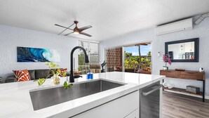 A modern kitchen with a large island, a ceiling fan, and a view of a tropical garden.