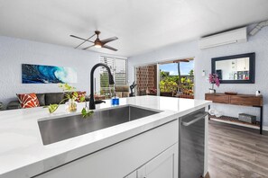 A modern kitchen with a large island, a ceiling fan, and a view of a tropical garden.