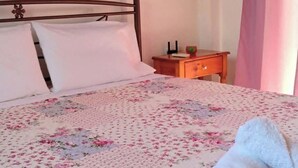 Un letto ben rifatto con una coperta a fiori, una testiera in legno, un comodino con una lampada e un quadro appeso al muro.