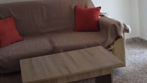 Un soggiorno con un divano, due cuscini rossi, un tavolino in legno e un quadro floreale appeso alla parete.