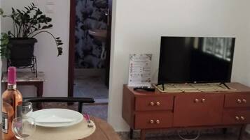 Ein Essbereich mit Tisch für zwei Personen, einem Fernseher auf einem Holzschrank und einer dekorativen Wanduhr.