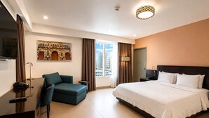 Una habitación de hotel con cama, escritorio, silla, televisor y ventana con cortinas.