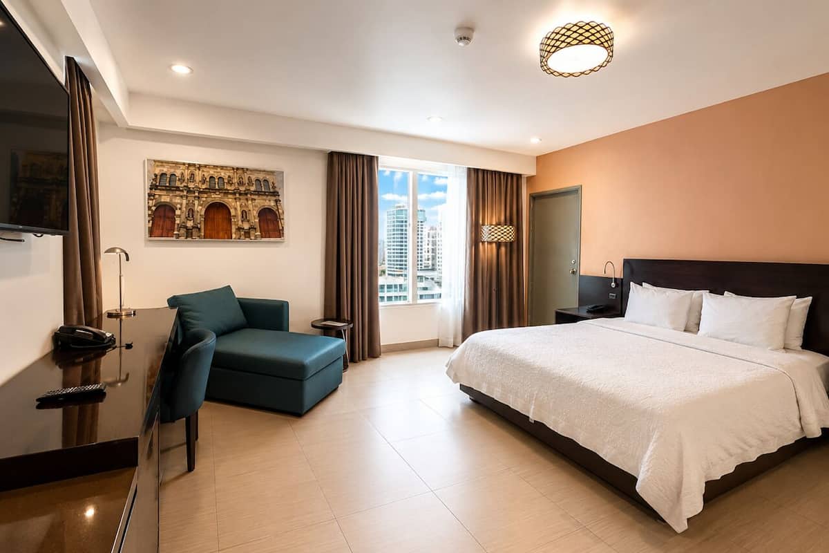 A hotel room with a bed, a desk, a chair, a TV, and a window with curtains.