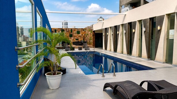 Una piscina en la azotea con sillas de descanso, una palmera en maceta y vistas a la ciudad.