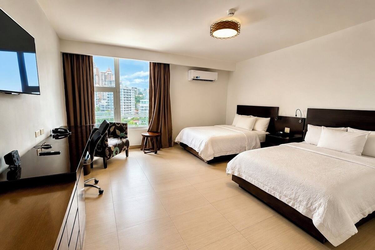 A hotel room with two beds, a desk, a chair, and a TV.