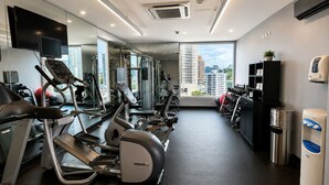Un gimnasio moderno con diversas máquinas de cardio, un muro de espejos y vistas a la ciudad.