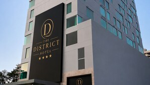 Un hotel moderno y alto con un letrero llamativo que dice 'The District Hotel' y un logotipo.