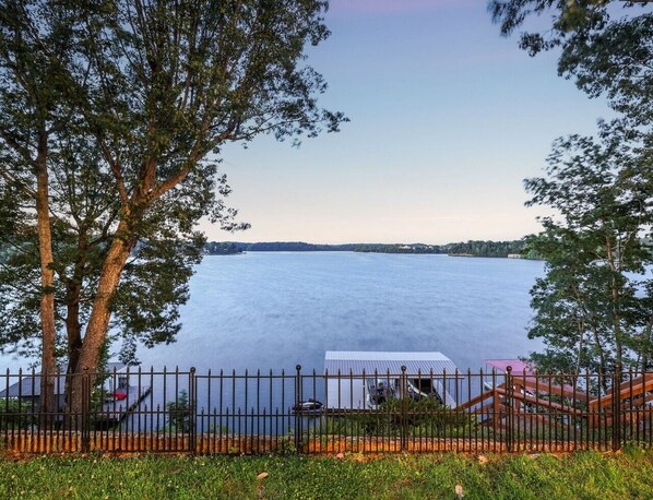 Vista de un lago con un muelle, un área cercada y un edificio con techo de metal.
