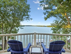 Une terrasse avec deux chaises et une table, donnant sur un lac où un bateau est amarré au loin.