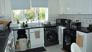 A kitchen with a washing machine, a sink, and a window with a view of greenery. - Whole Cosy Home, Sleeps 11 in 4 Bedrooms, full kitchen, 2 toilets, 55"TVs PetsOK (Wolverhampton)
