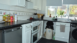 A kitchen with white cabinets, a dishwasher, an oven, a sink, and a window with a view of trees. - Whole Cosy Home, Sleeps 11 in 4 Bedrooms, full kitchen, 2 toilets, 55"TVs PetsOK (Wolverhampton)