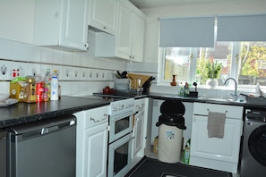 Una cocina con armarios blancos, lavavajillas, horno, fregadero y ventana con vista a árboles.