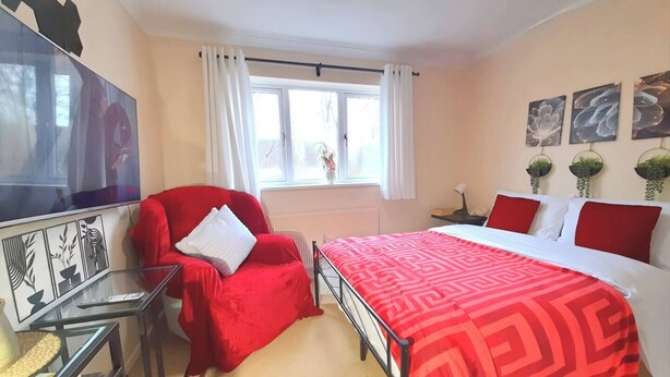 A bedroom with a bed, a red armchair, a TV, and a window with curtains. - Whole Cosy Home, Sleeps 11 in 4 Bedrooms, full kitchen, 2 toilets, 55"TVs PetsOK (Wolverhampton)