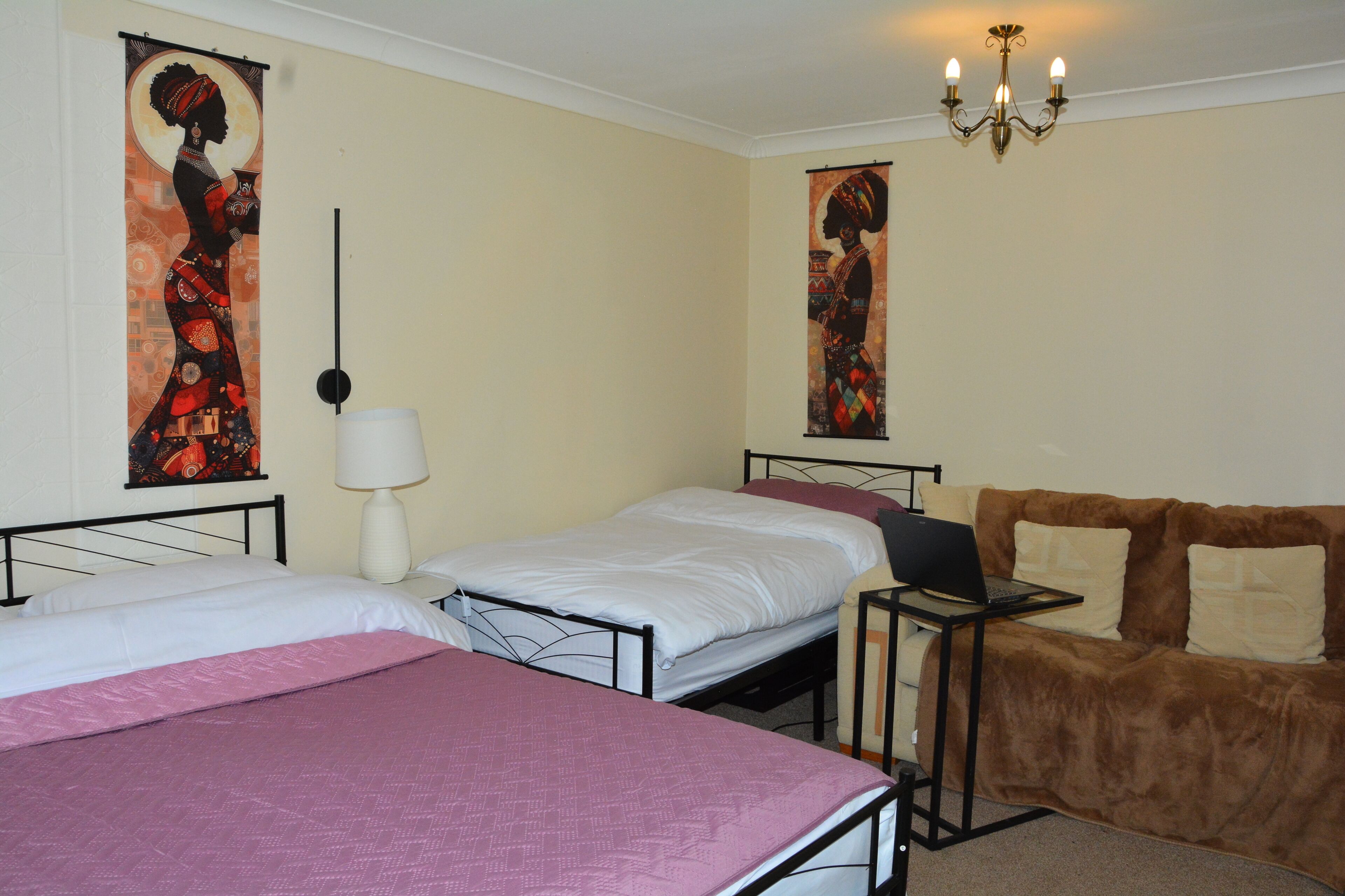 A room with two beds, a desk with a laptop, a couch, and two wall-mounted artworks.