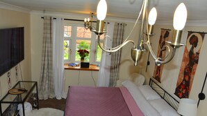 A bedroom with a bed, a chandelier, a window with curtains, a TV, and artwork on the wall. - Whole Cosy Home, Sleeps 11 in 4 Bedrooms, full kitchen, 2 toilets, 55"TVs PetsOK (Wolverhampton)