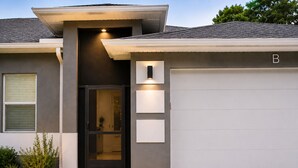 A modern house with a garage, a front door, and a small garden. - Family Friendly SWFL Home• 3BR, Sleeps 6, Screened Lanai (Fort Myers)