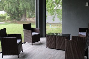 Un espace extérieur moderne aménagé avec des meubles en osier et une table en verre, offrant une vue sur un jardin.