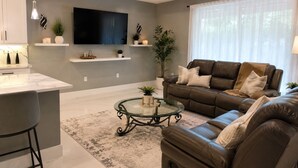 A modern living room with a sofa, coffee table, TV, and plants. - Family Friendly SWFL Home• 3BR, Sleeps 6, Screened Lanai (Fort Myers)