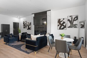 Ein modernes Wohnzimmer mit einem dunkelblauen Sofagarnitur, einem runden Esstisch mit grauen Stühlen und abstrakter Kunst an den Wänden.