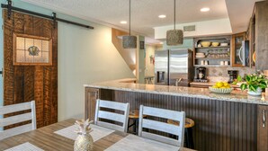 A kitchen with a central island, wooden cabinets, and a dining area with a table and chairs. - Ocean Views, Two Balconies, Easy Beach Access, Two Pools, 5 miles to Downtown, $300 in Free Tickets! (St. Augustine Beach)