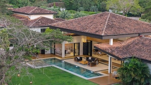 Uma casa moderna com piscina, um alpendre com móveis de exterior e um jardim exuberante.