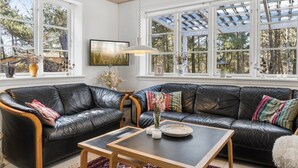 A living room with a black leather sofa, a wooden coffee table, and a TV mounted on the wall. - "Mirzə" - 180m from the sea by Interhome (Rønne)