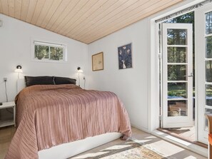 Ein Schlafzimmer mit einem Bett, zwei Nachttischlampen, einem Fenster und einer Tür, die nach draußen führt.