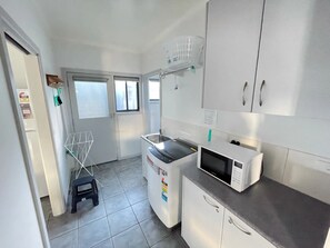 A compact kitchen with a washing machine, a microwave, and a small window.