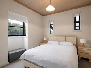 A bedroom with a bed, bedside tables, a bench, and windows.
