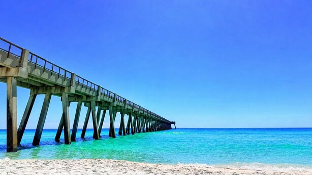 Eine Steg, der sich in ein klares, blaues Meer erstreckt, mit einem Sandstrand am Ende.