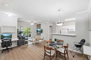 Un salon moderne comprenant un canapé, un téléviseur et un coin repas avec des chaises et une table.