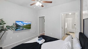 Ein Schlafzimmer mit einem Bett, einem Deckenventilator, einem an der Wand befestigten Fernseher und einer Tür zu einem Badezimmer.
