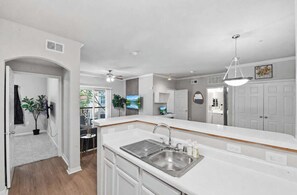 Une cuisine moderne avec des meubles blancs, un évier en acier inoxydable et un ventilateur de plafond.