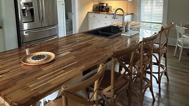 Een keuken met een houten eiland, roestvrijstalen apparatuur en rieten stoelen.