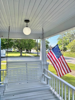 A porch with a white railing, a hanging American flag, and a hanging light fixture. - Historic River House with Sunrise Views (New Bern)