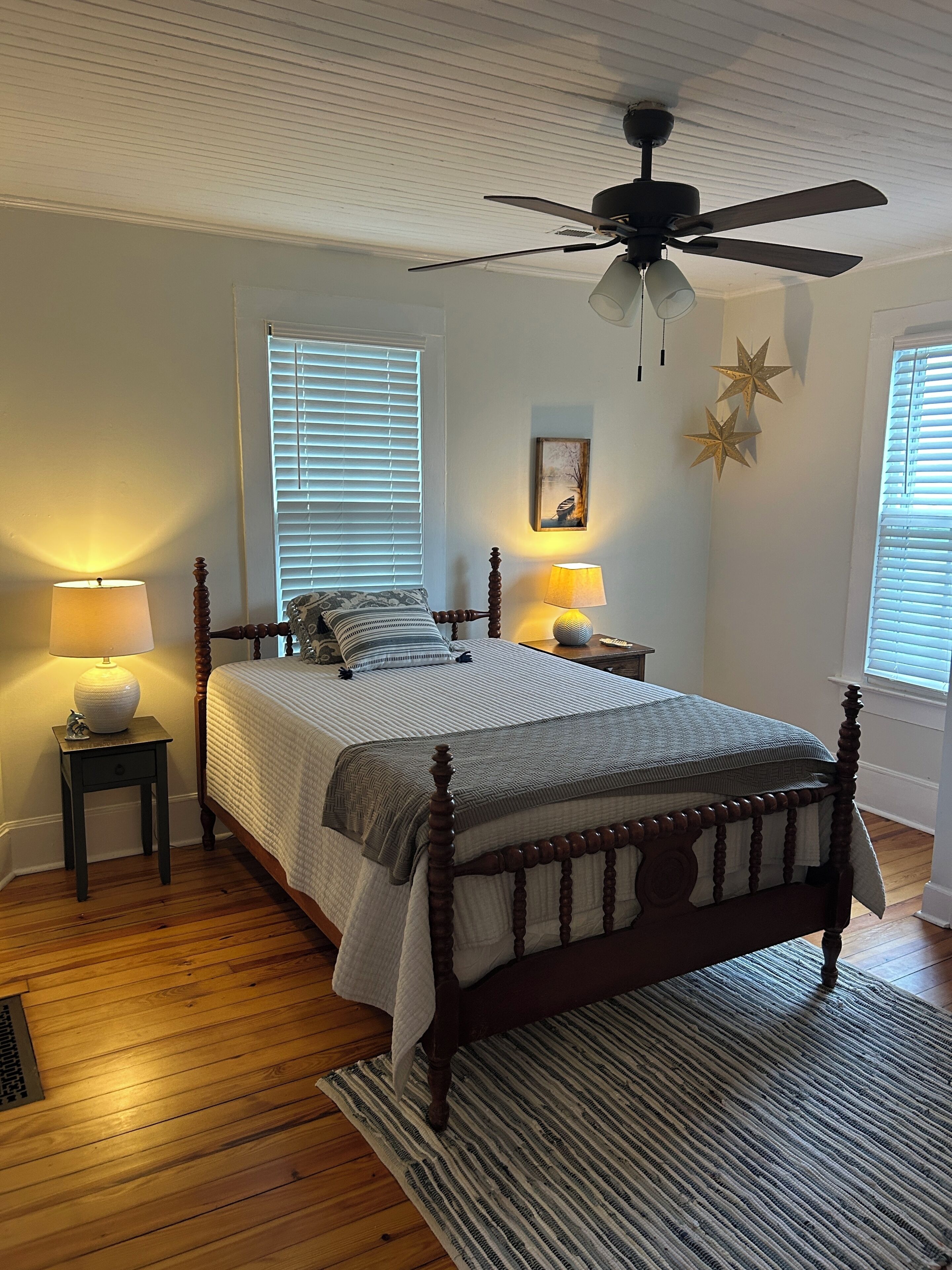 A bedroom with a wooden bed, two bedside lamps, a ceiling fan, and a window with blinds.